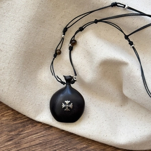 Detail of a dark wood pendant necklace with a vintage silver cross inlay and beads