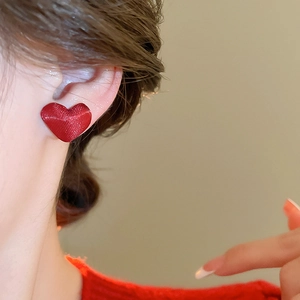Dettaglio di una modella che indossa un orecchino a cuore rosso vivo con texture in tessuto