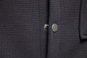 Macro shot of dark grey waffle fabric texture and metal snap buttons on men jacket