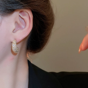Detailed close-up of crescent gold stud earring with zircons worn by model in black suit