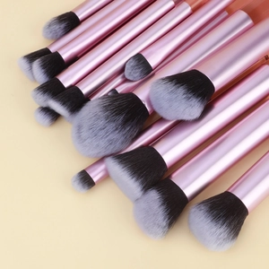 Détail de 16 pinceaux de maquillage roses avec poils dégradés sur fond jaune clair