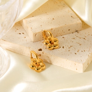 Detailed view of 18K gold plated flower earrings on textured beige stone surfaces