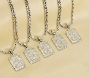 Detailed view of silver square letter pendants A to E on elegant silk fabric