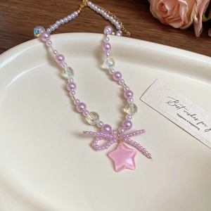 Detail shot of a pink star pendant and bow on a beaded pearl necklace for women