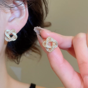 Close-up of gold-plated knot earrings with zircons shown on ear and held by hand