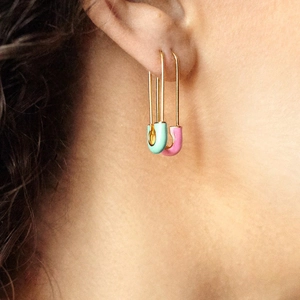 Close-up of mint green and pink enamel safety pin earrings on a female model ear