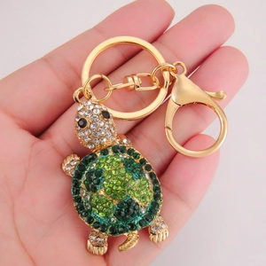 Close-up of golden turtle keychain with green and white rhinestones held in hand