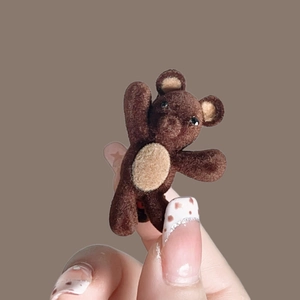 Gros plan détaillé d'une pince à cheveux ours floqué marron tenue à la main sur fond brun