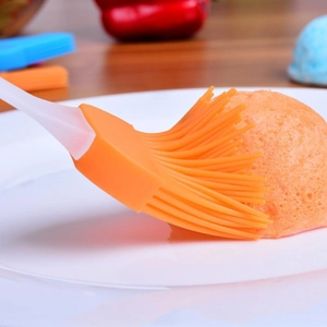 Heat-resistant silicone basting brush with orange bristles for BBQ and baking on white plate