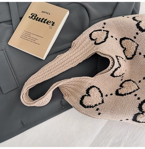 Détail du sac fourre-tout beige en maille avec motif cœur sur fond de blazer gris