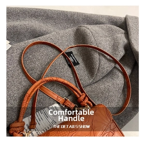 Détail de la texture du cuir marron gaufré et de la poignée nouée tressée du sac à main