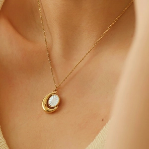 Minimalist gold moon and sun necklace with white shell pendant worn by a female model