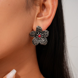 Detail von schwarzen Diamant-Blumenohrringen mit roter Perle an einem Model