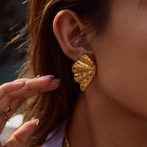 Close-up of elegant gold shell earrings with pearl details on a model for a luxury look