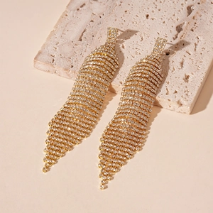Détail de boucles d'oreilles pompons dorées avec strass brillants sur socle en pierre