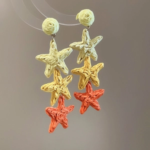 Detail of woven raffia star earrings showing tiered texture and yellow-orange gradient
