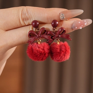 Detail shot of red plush ball bow earrings featuring a gold-toned metal connector