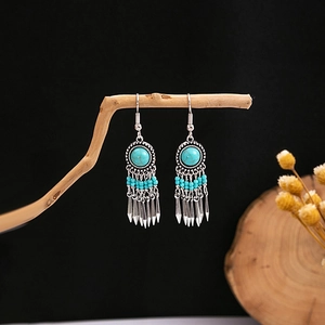 Detail of bohemian silver earrings with turquoise stones and blue tassel on wood branch