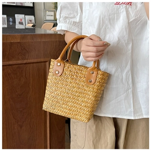 Minimalist straw handbag with brown leather handles held in a natural home setting