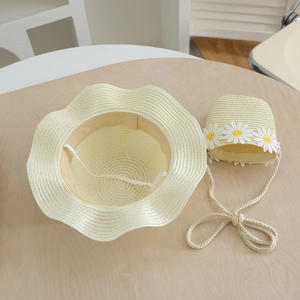 Straw sun hat and matching crossbody bag set with white daisy accents on wood background