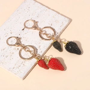 Macro view of red and black strawberry keychain charms on a textured white stone