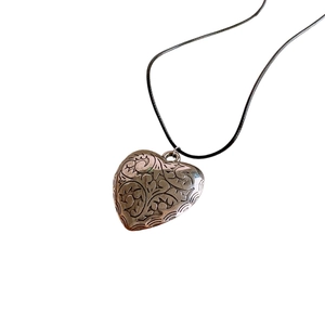Vintage heart pendant necklace with carved floral details and black cord on white background