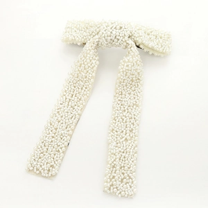 Detailed close-up of handmade white faux pearl and bead bow hairpin with long tassel
