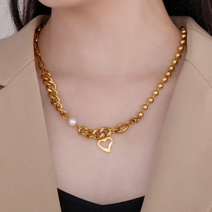 Gros plan du collier coeur doré avec chaîne cubaine asymétrique et perle élégante