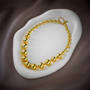 Elegant gold beaded titanium steel necklace displayed on a white stand over grey silk fabric
