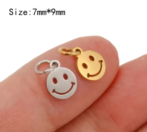 Macro view of tiny gold and silver smiley face charms on a fingertip for size scale