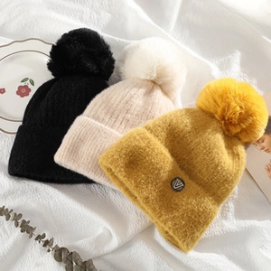 Detailed close-up of knitted beanies in black, cream, and yellow with fluffy faux fur pom-poms