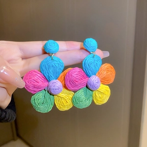 Handheld close-up showing colorful woven raffia flower earrings in vibrant summer shades