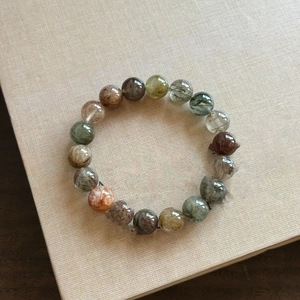 Macro detail of mixed rutilated quartz beaded bracelet on a minimalist textured surface