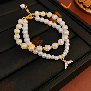 Detail of gold plated double-layer pearl bracelet with a shimmering fishtail pendant