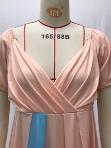 Détail d'une robe rose avec décolleté en V profond, plis drapés et bordure bleue