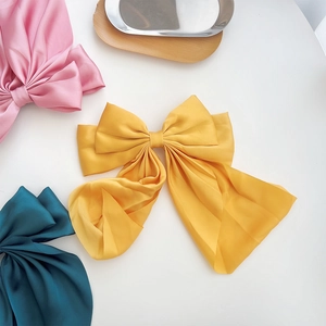 Three oversized silk bow hair clips in yellow, pink, and dark green on a metal tray