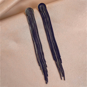 Detail of elegant gold and dark blue layered chain tassel earrings on beige satin