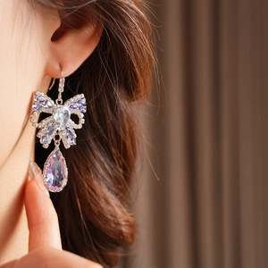 Close-up of elegant silver bow drop earrings with purple crystals on a female model