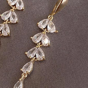 Macro shot of gold tassel drop earrings with sparkling teardrop crystals on grey fabric