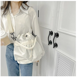 Close-up of white nylon drawstring bucket bag with beige strap and minimalist hardware