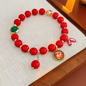 Détail macro du bracelet perlé rouge avec pendentif phénix doré et breloque en gemme