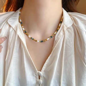 Detail of multi-color beaded necklace featuring green, gold, and white shell pearls