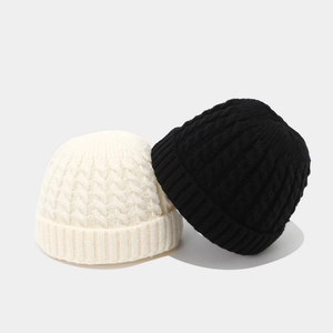 Close-up of knit cable texture on white and black beanies with thick folded cuffs