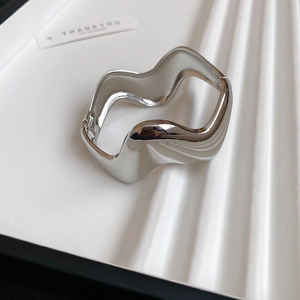 Macro detail of silver irregular wavy cuff bracelet with polished mirror surface and hinge