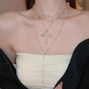 Macro detail of layered gold-tone necklace with rhinestone cross and star pendants