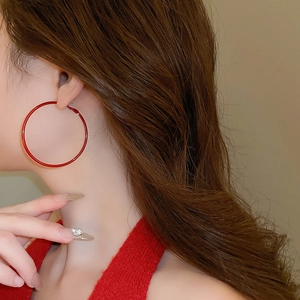 Close-up of large red enamel hoop earring worn by a model in a minimalist setting