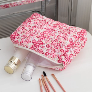 Detailed view of quilted floral makeup bag with metal zipper on a white surface