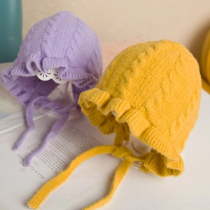 Detail of baby knitted earflap hats with ruffle lace and braided texture in purple and yellow