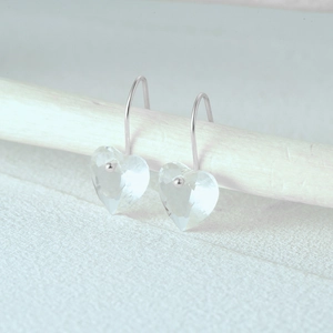 Detailed view of heart-shaped crystal drop earrings on elegant white wood background