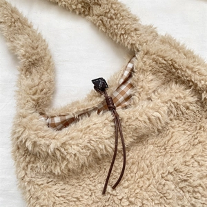 Detail of plush faux fur shoulder bag featuring brown checkered lining and drawstring closure